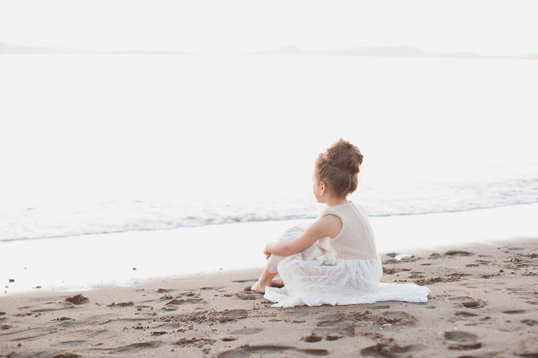 little girl in white dress looking out to the ocean