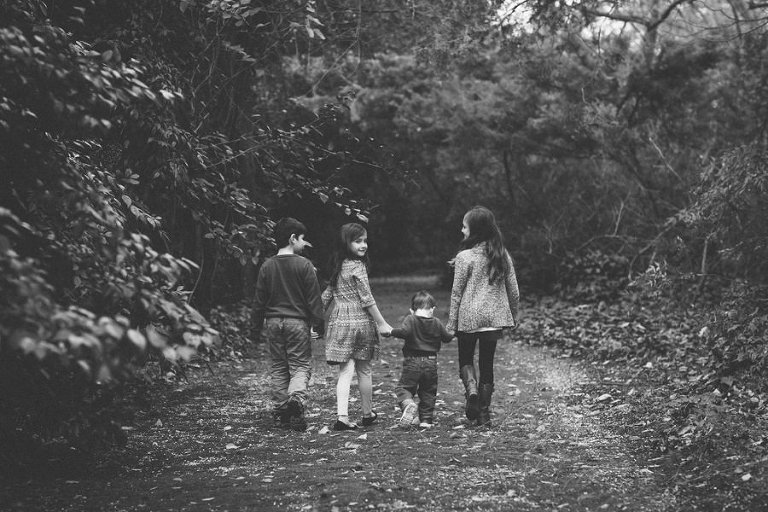 black and white photo of four cousins holding hands walking away from the camera