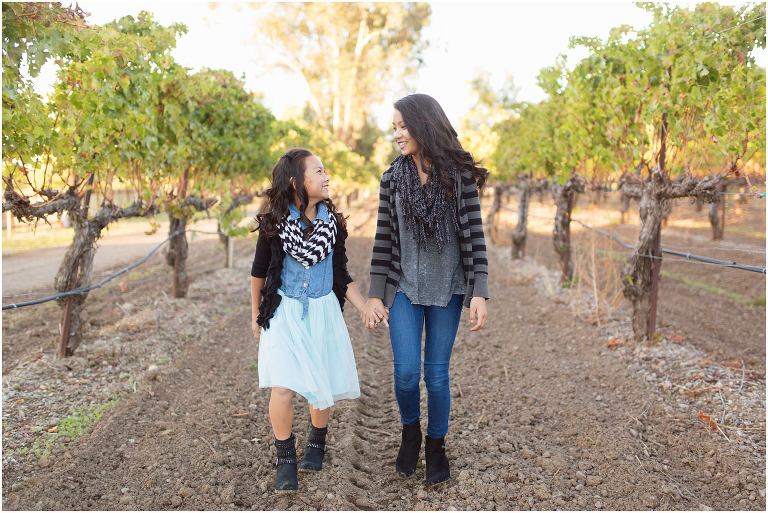 sisters walking hand in hand in row of grapevines