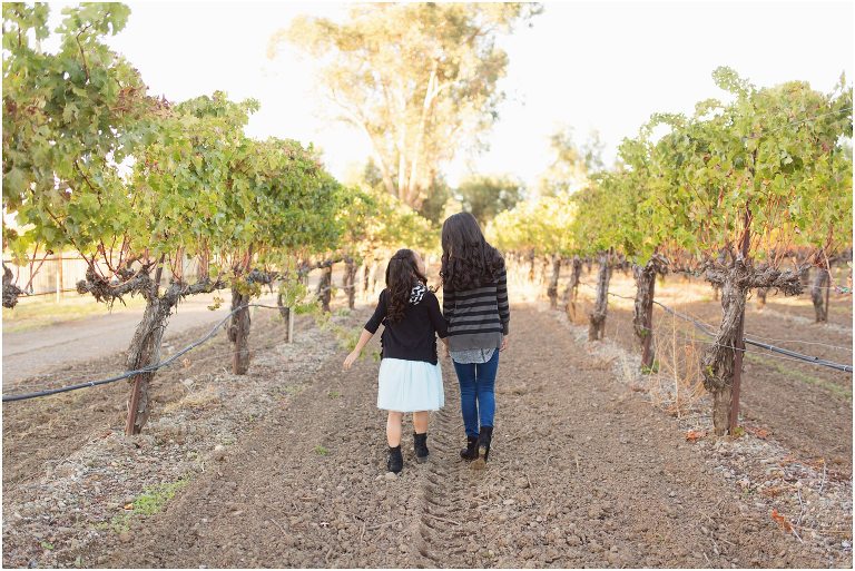 sisters walking away from the camera in row of grapevines