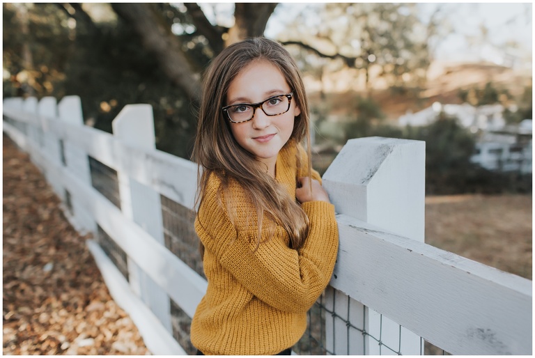 headshot of girl leaning against fence wearing glasses 