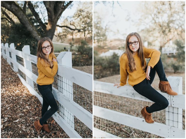 little girl sitting on white fence in mustard sweater